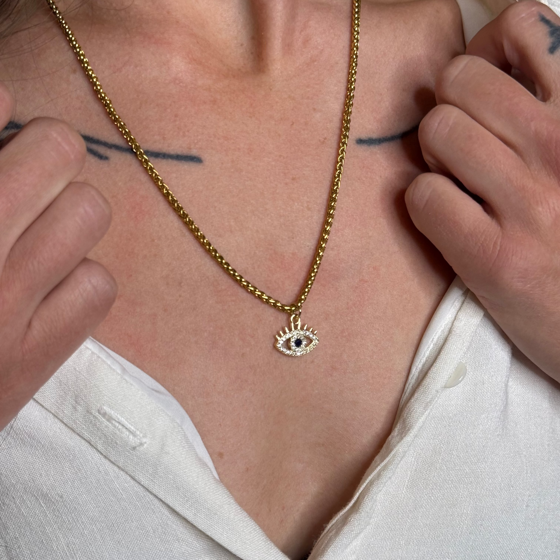 Person wearing a gold necklace with an eye pendant, close-up on neck and chest.