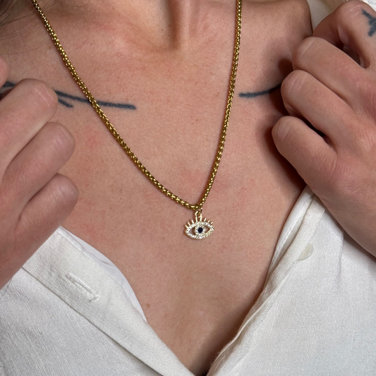 Person wearing a gold necklace with an eye pendant, close-up on neck and chest.