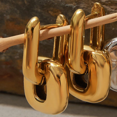 Gold and silver hoop earrings on a wooden stick against a stone background